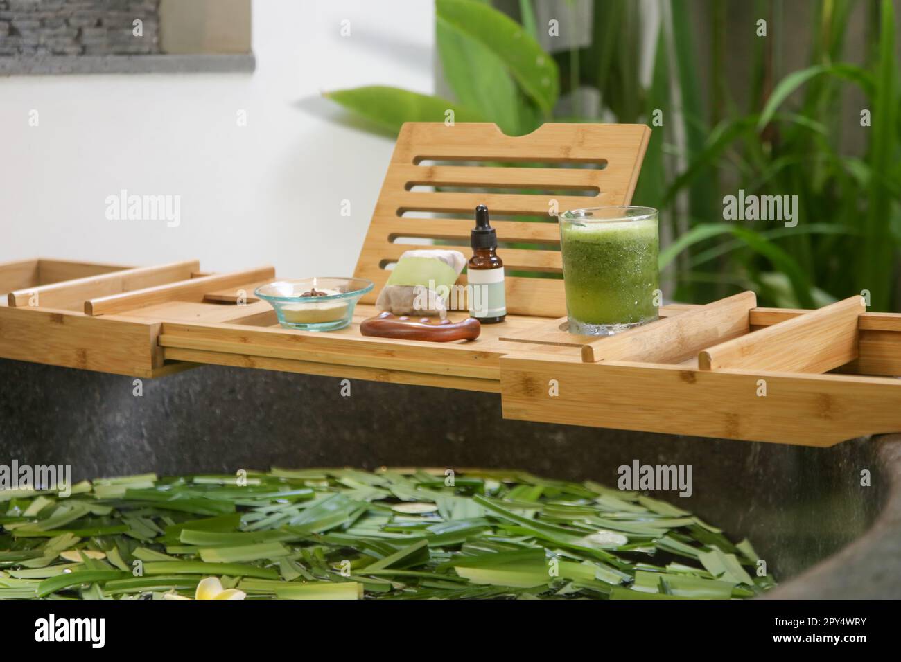 Tub full of water and herbs with wooden bathtub tray with various