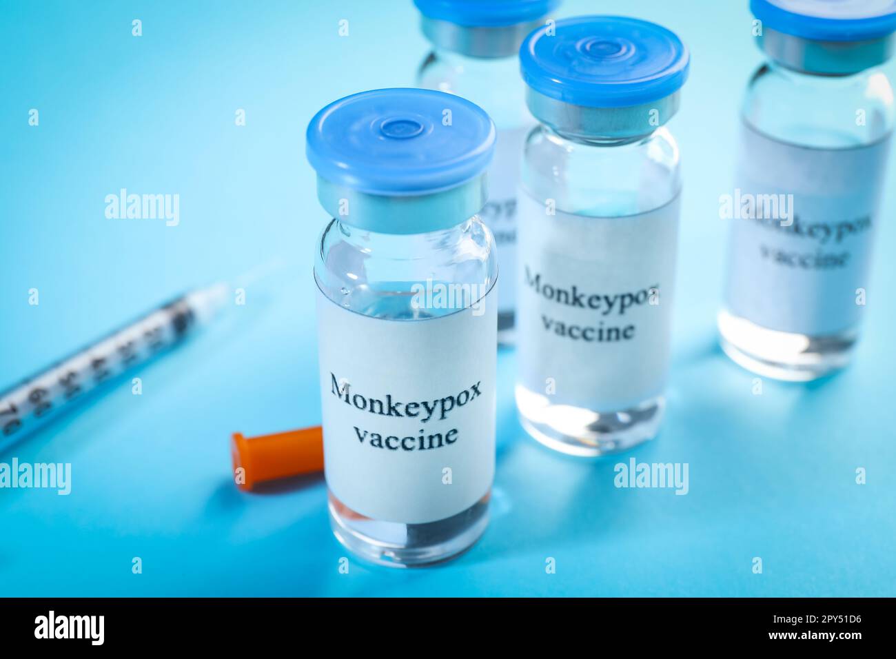 Monkeypox vaccine in glass vials and syringe on light blue background ...