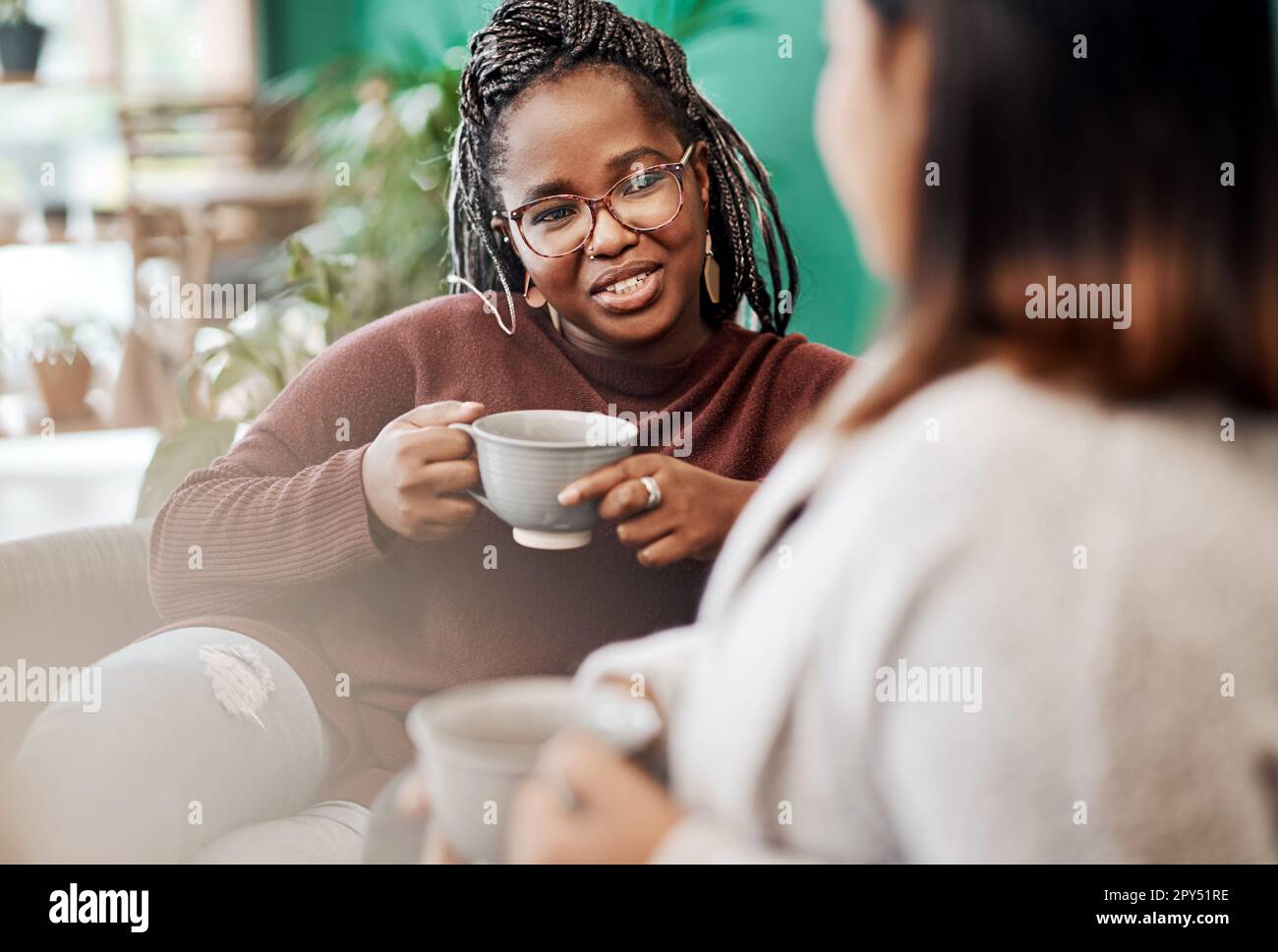 Coffee, the official drink of girls night in. two young women having coffee  and chatting on the sofa at home Stock Photo - Alamy