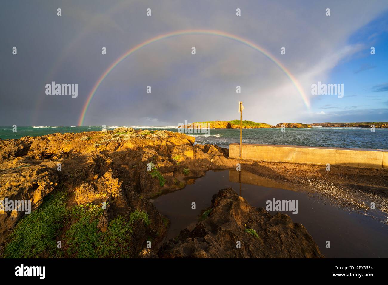 A double rainbow in front of a dark storm cloud over a rocky coastline at Warrnambool on the Great Ocean road in Victoria, Australia Stock Photo