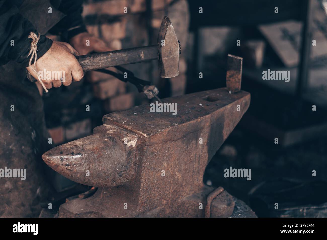 Blacksmith working metal with hammer and pincers on anvil in forge. Farrier strike iron in workshop. Metalworking. Stock Photo