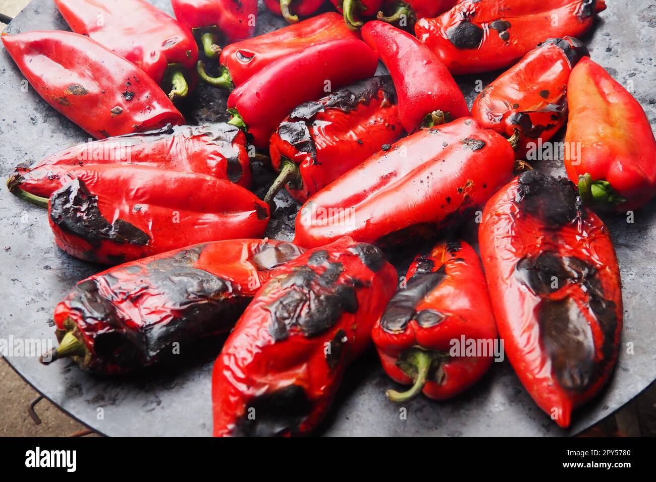 Roasting delicious red peppers for a smoky flavor and quick peeling. Balkan salad recipes. Thermal processing of the pepper crop on a metal circle. Peppers are laid out on a flat baking sheet closeup Stock Photo
