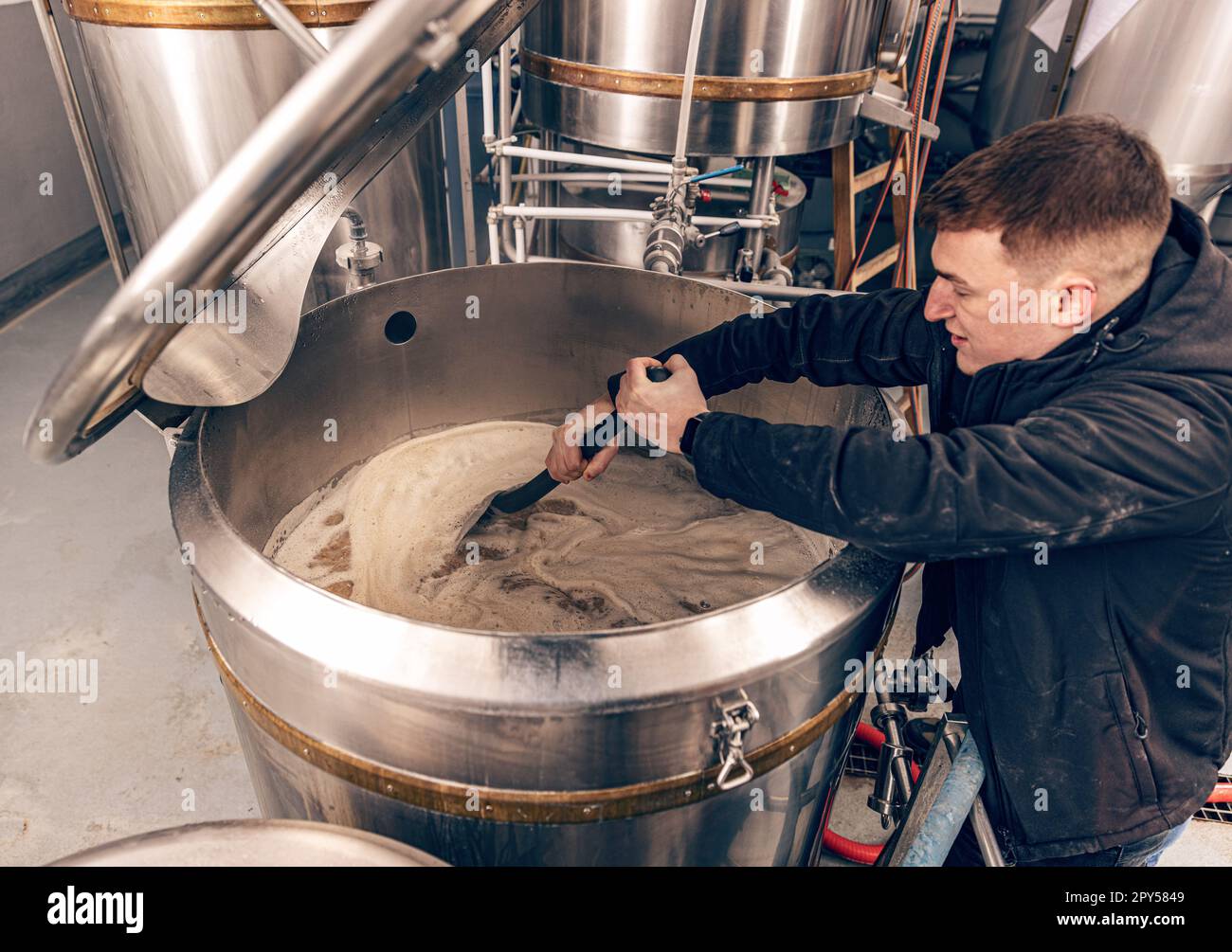 Brewery worker controlling process of craft beer production, stirring