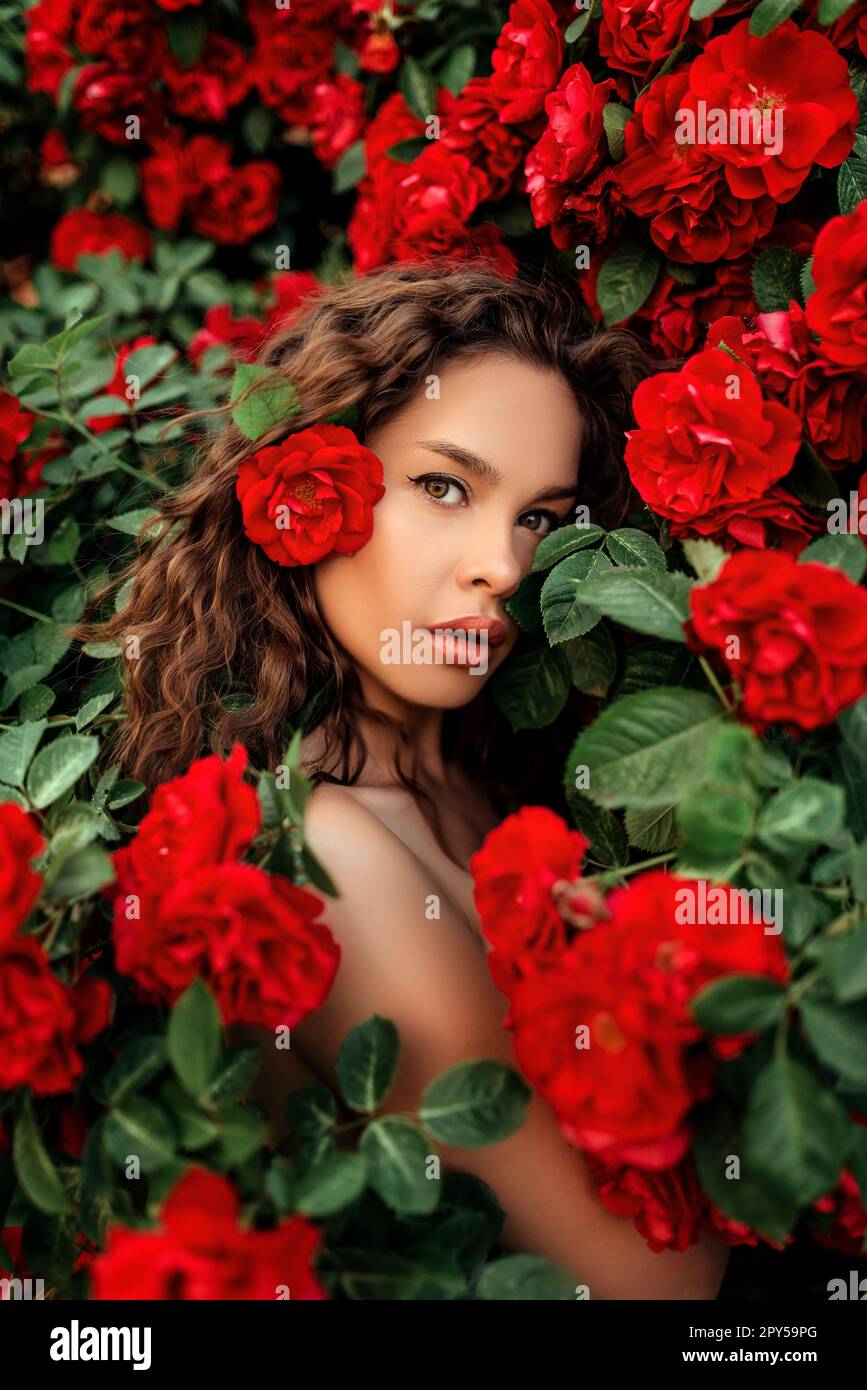 Girl in red dress and straw hat in garden with red roses. Gardening Stock Photo