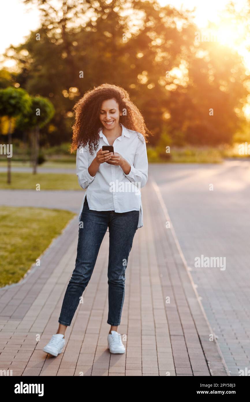 A young girl walks in the park and uses social networks using a mobile phone. Stock Photo