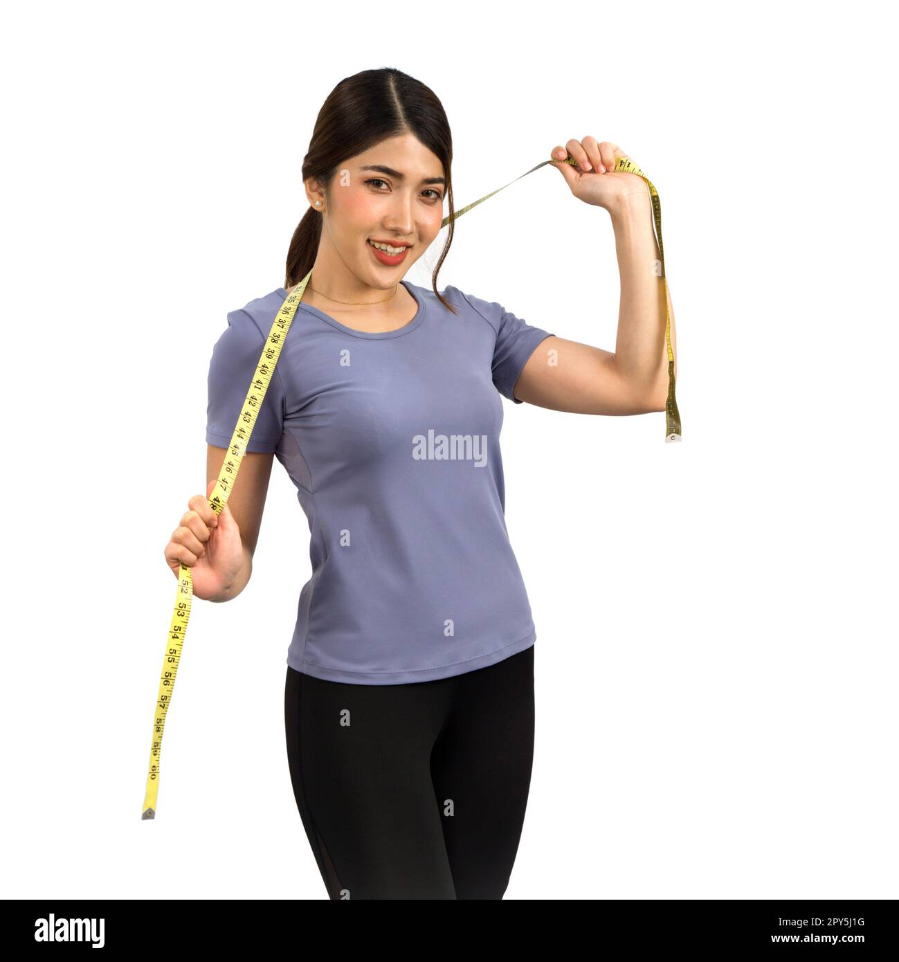 Young Asian woman in fitness clothes holding a measuring tape with a smile. Portrait on white background with studio light. Healthy nutrition and weight losing concept. Stock Photo