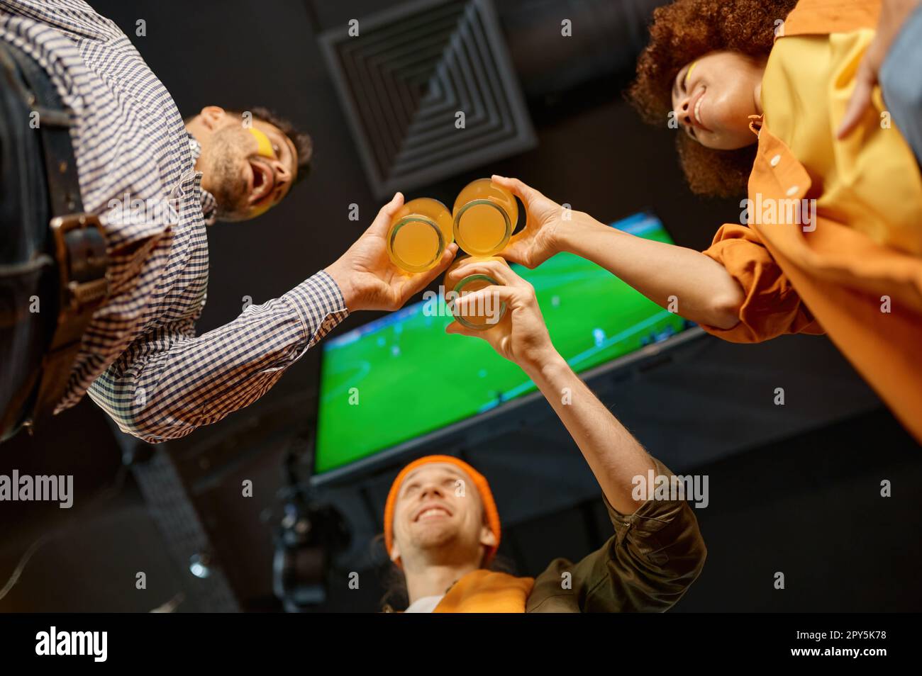 Group of friends celebrating win clinking beer glasses in sports bar Stock Photo