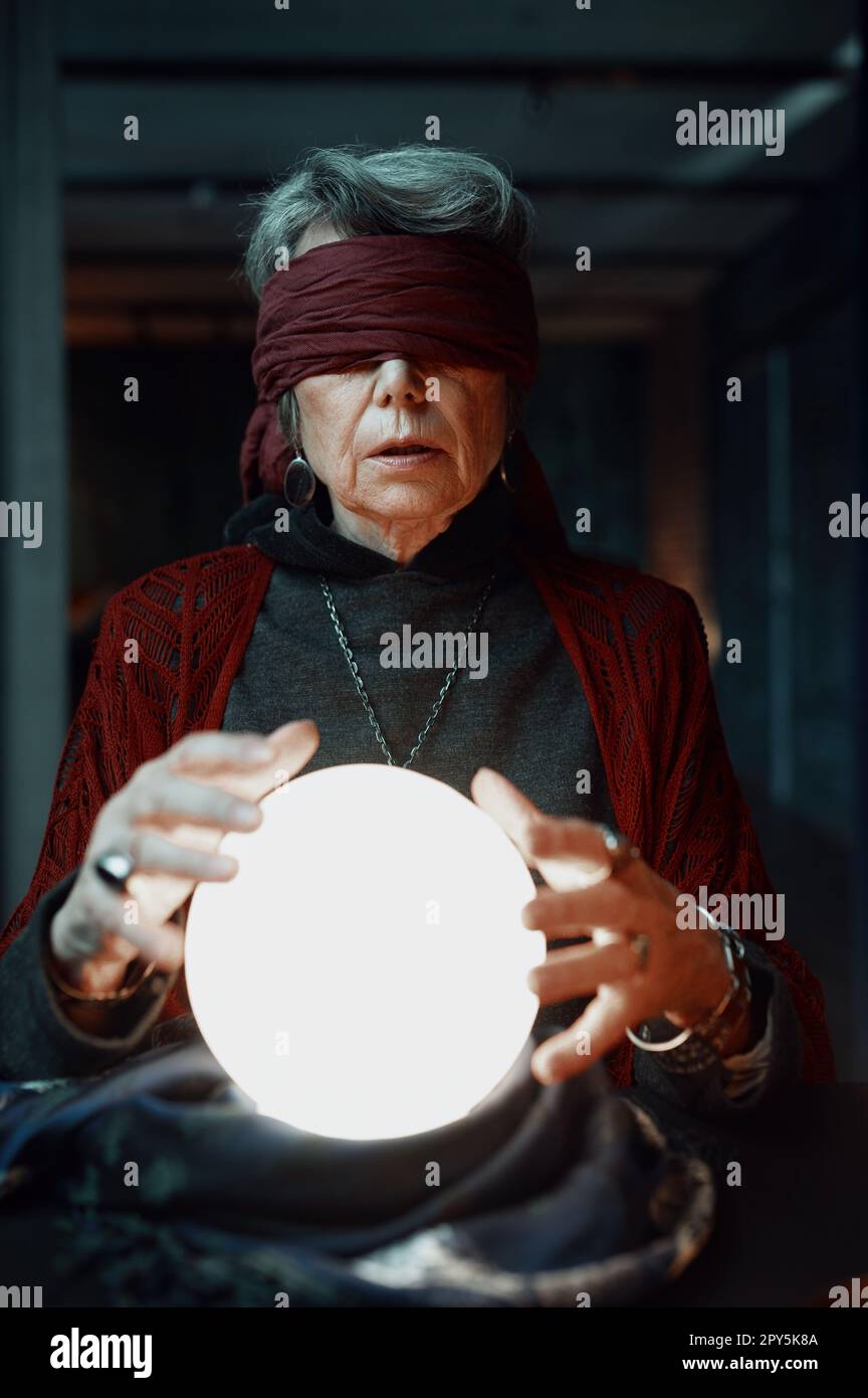 Blindfolded witch fortune teller doing predictions with illuminated crystal ball Stock Photo
