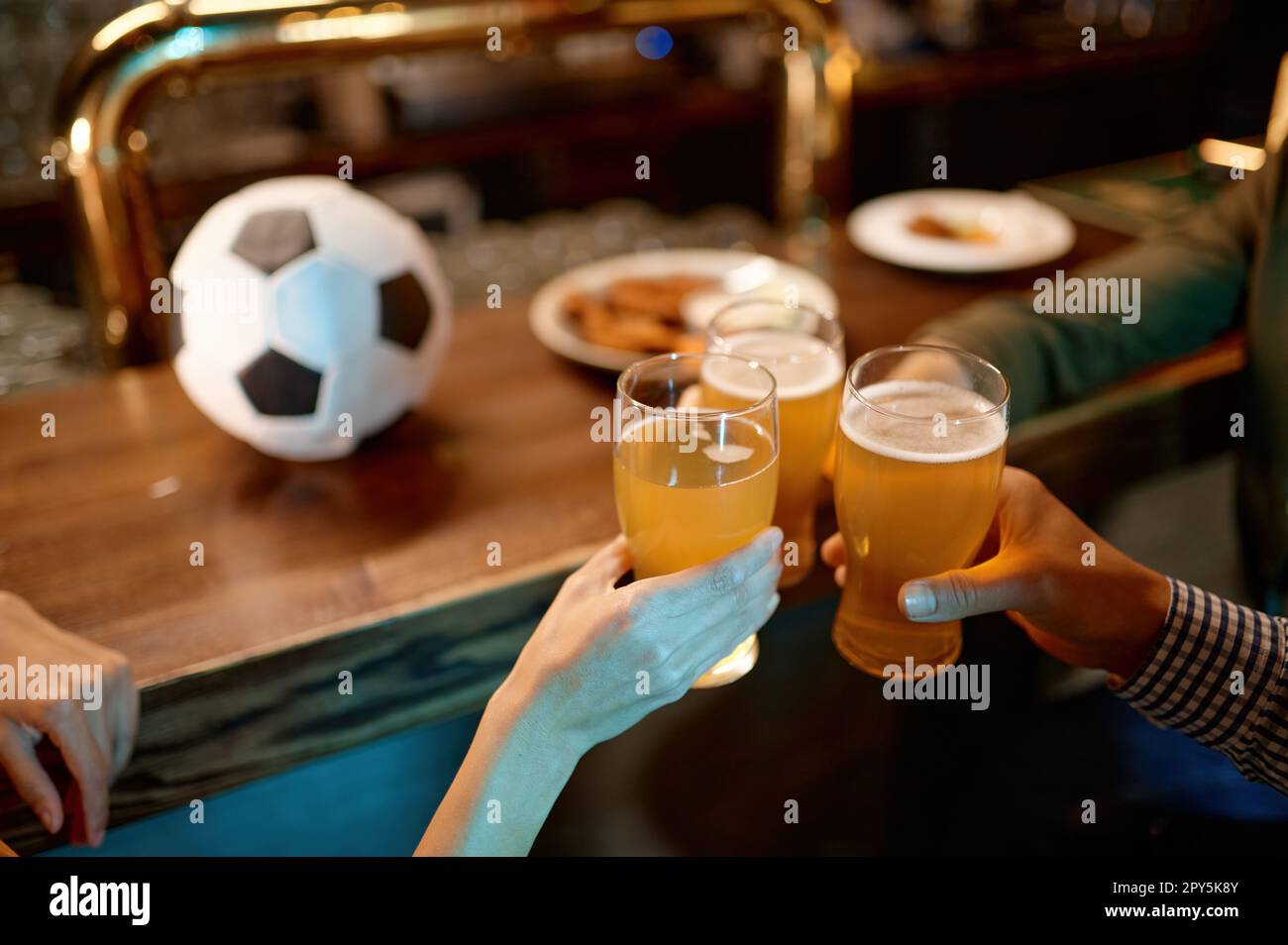 Closeup friends football fans clinking beer glasses at sport bar or pub Stock Photo