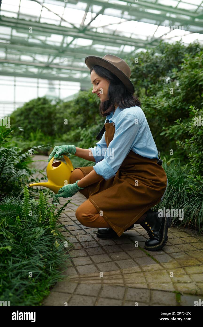 Young woman gardener with watering can caring for plants in hothouse Stock Photo
