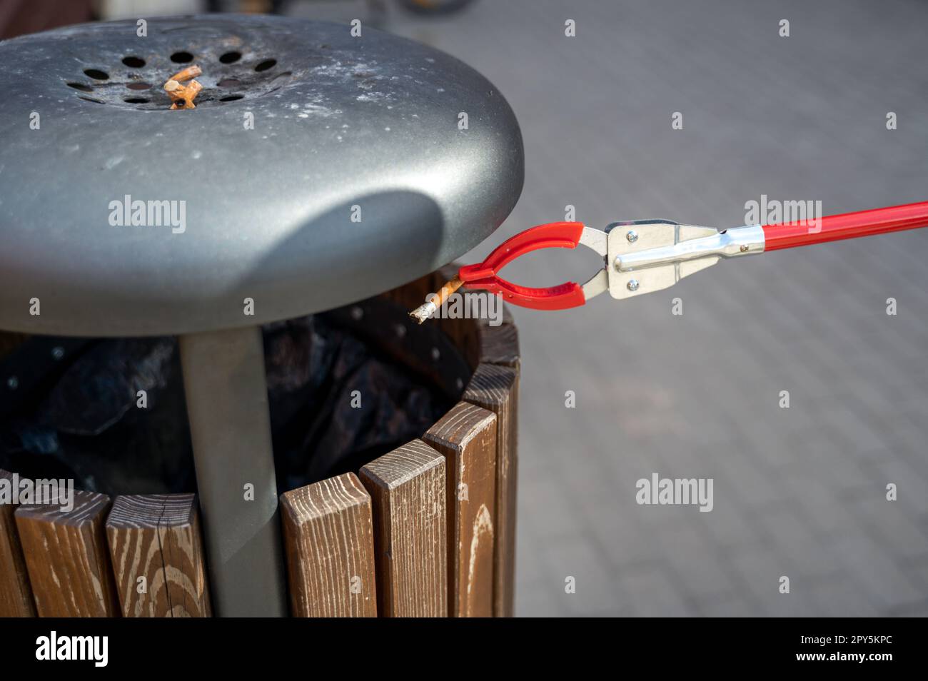 Person with Grabber Reacher Tool putting cigarette butts from ground ...