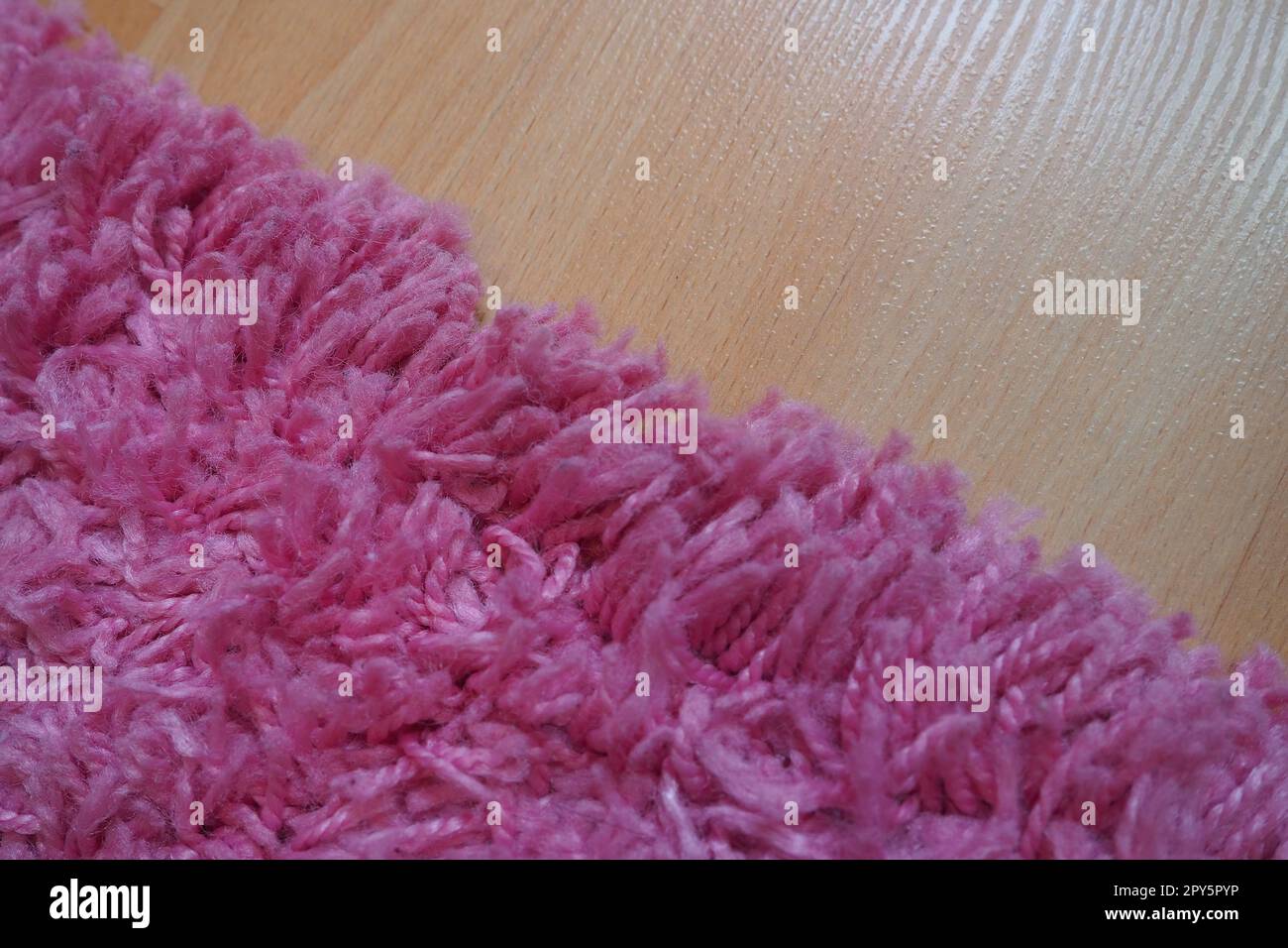 Long pile rug in pink on a beige laminate floor. Feminine interior for a room or bedroom of a girl or woman. Interior design in pink tones. Flooring is laminate. The role of dust mites in allergies. Stock Photo