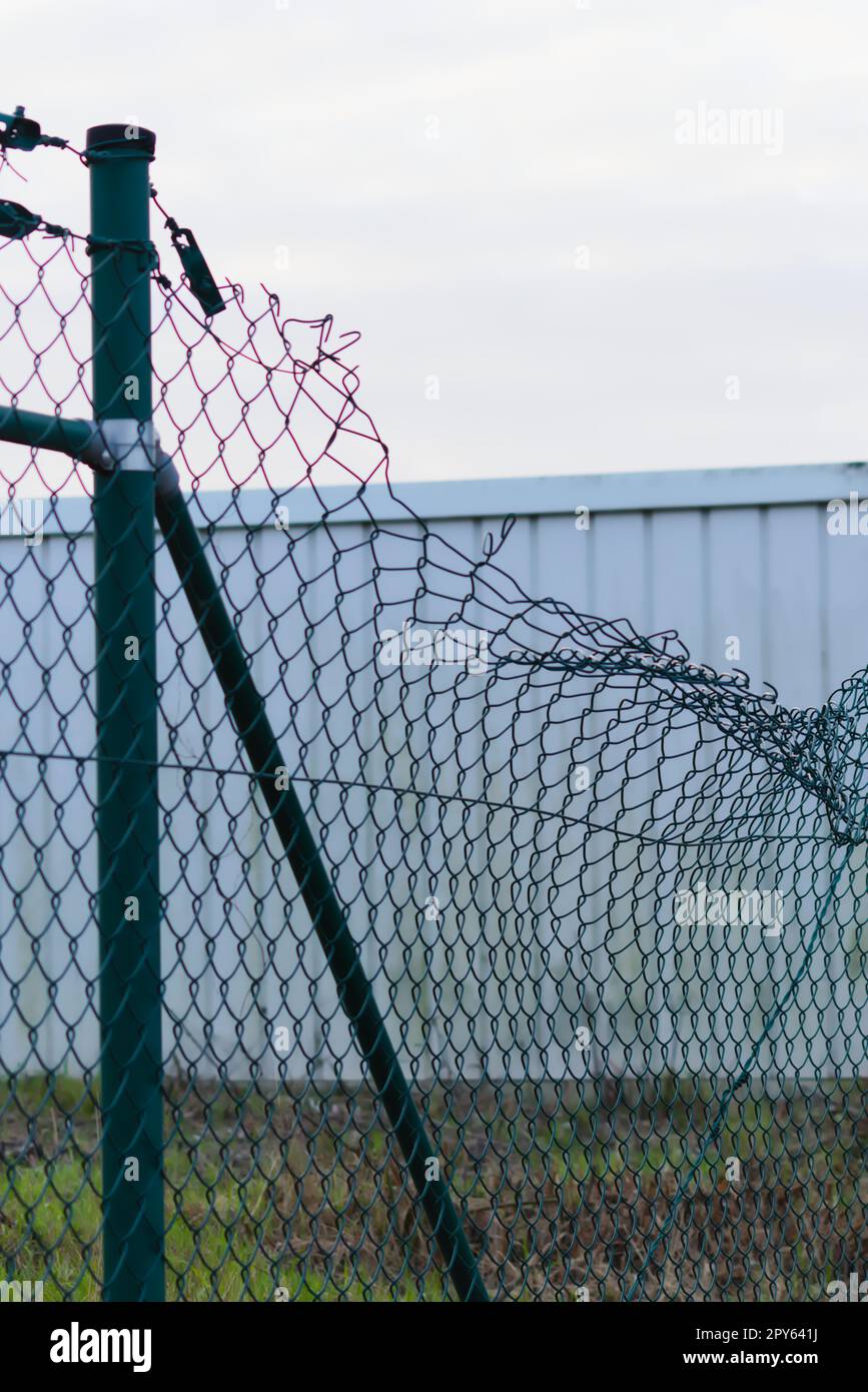 Green damaged wire-mesh fence is ruined after collision with car accident as crushed fence for car insurance and property insurance and loses security and safety with vandalism and barrier demolition Stock Photo