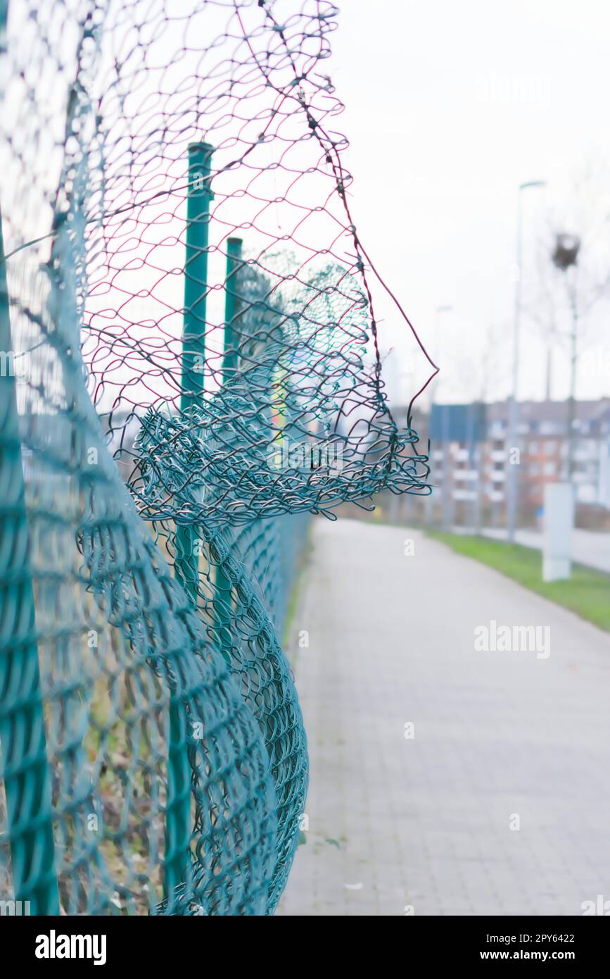 Green damaged wire-mesh fence is ruined after collision with car accident as crushed fence for car insurance and property insurance and loses security and safety with vandalism and barrier demolition Stock Photo
