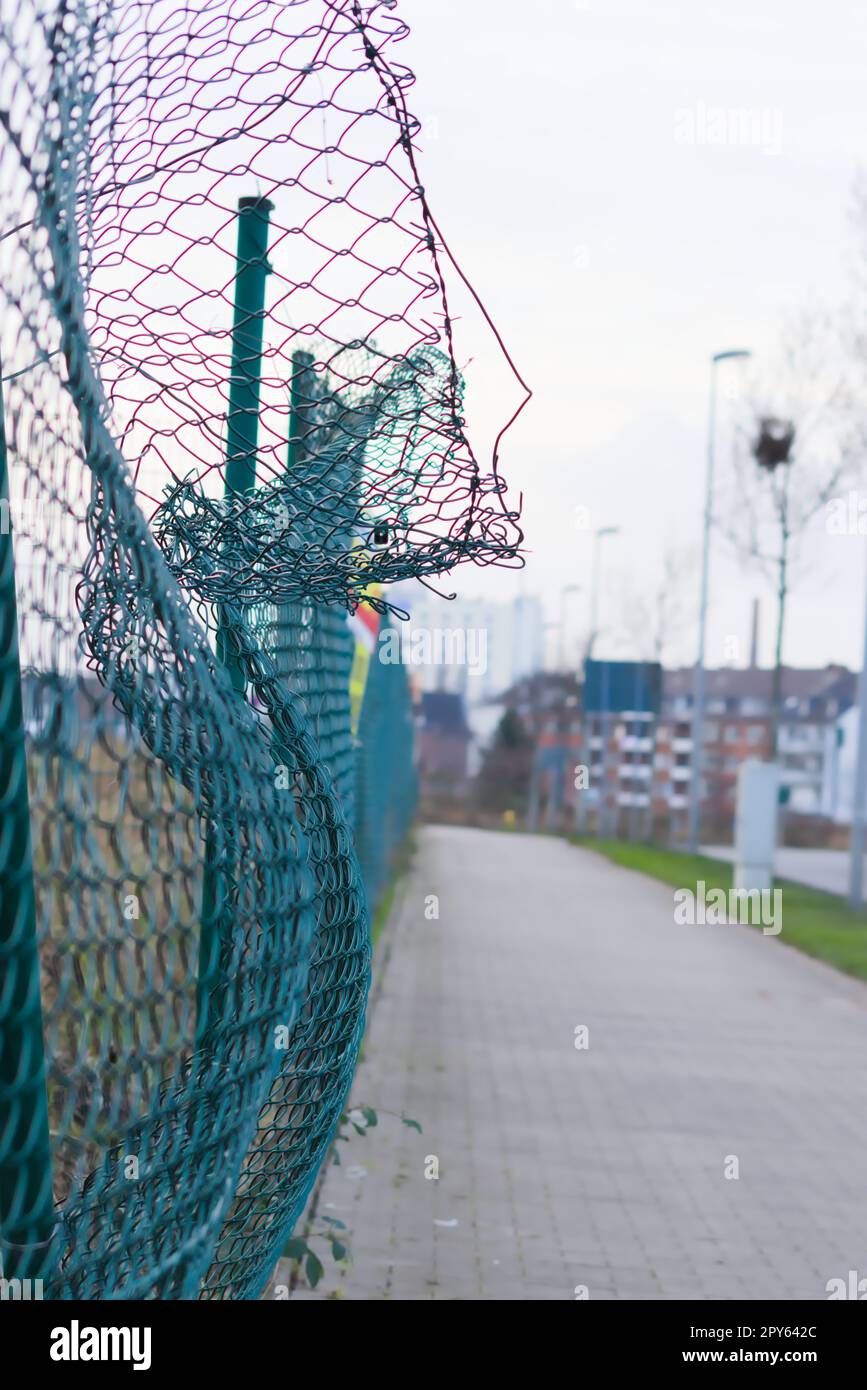 Green damaged wire-mesh fence is ruined after collision with car accident as crushed fence for car insurance and property insurance and loses security and safety with vandalism and barrier demolition Stock Photo