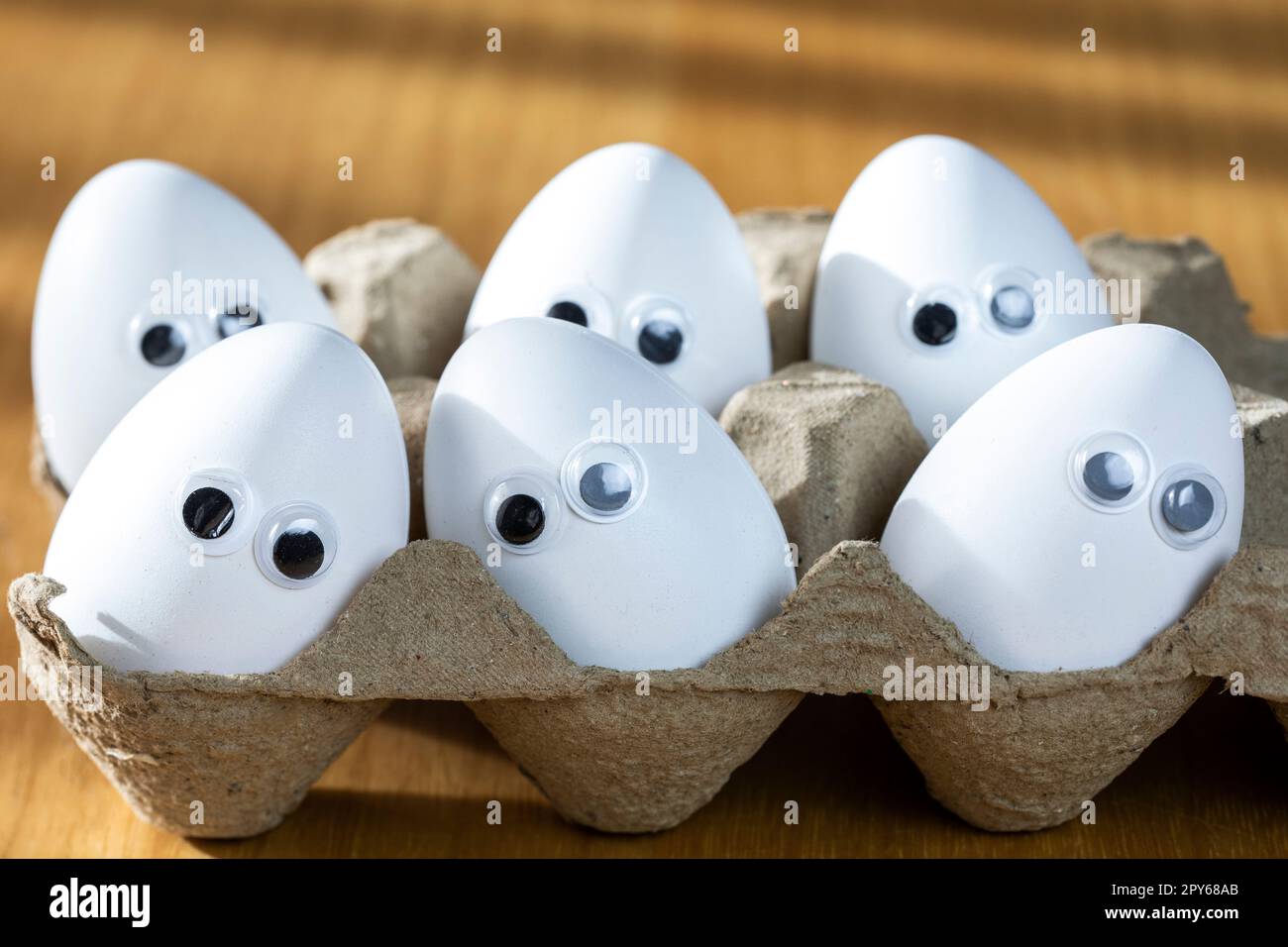 Funny faces on white eggs in carton box with organic chicken eggs on kitchen table closeup big animation eyes. humor, food and easter holiday concept. Stock Photo