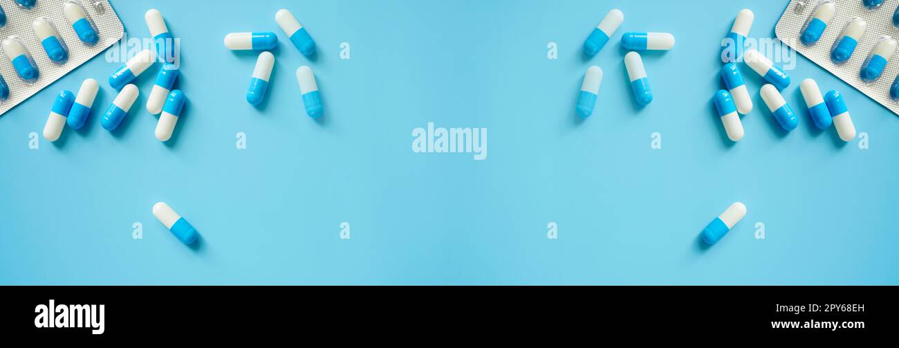 Blue-white antibiotic capsule pills and pill blister pack on blue background. Online pharmacy banner. World Health Day. Pharmaceutical industry. Prescription drugs. Antibiotic drug resistance concept. Stock Photo
