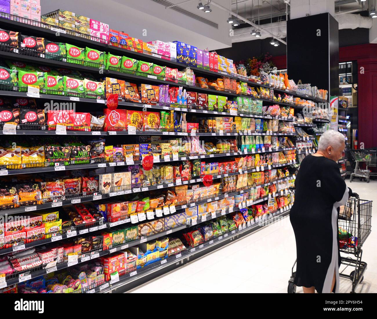 Biscuit aisle, kitkats prominent, older woman looks at products. Food supermarket at the Siam