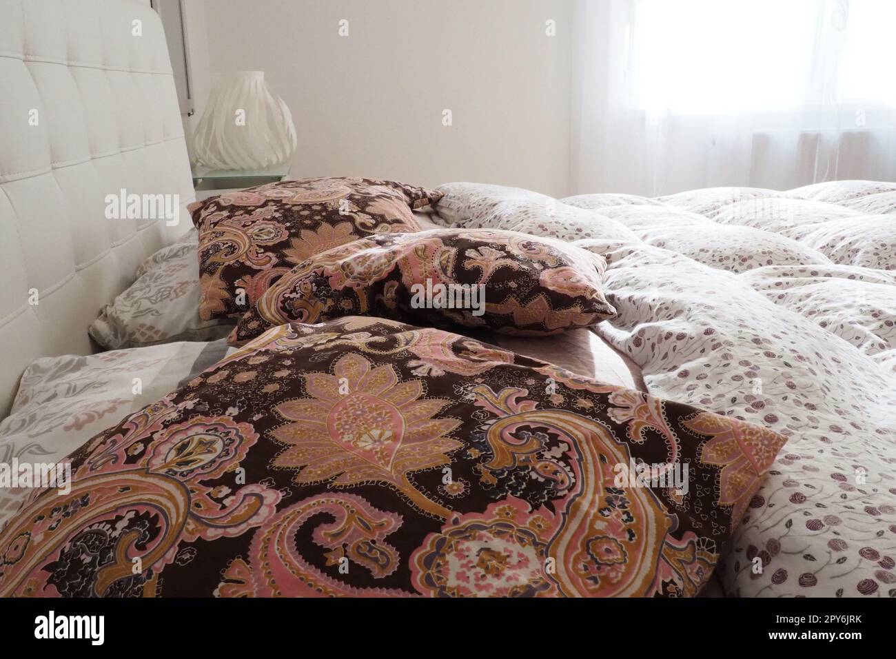 Pink decorative pillows on the bed linen. Double bridal bed with pillows and thick feather duvet. Bedroom design. Soft white headboard. Interior with furniture and bedding. Stock Photo