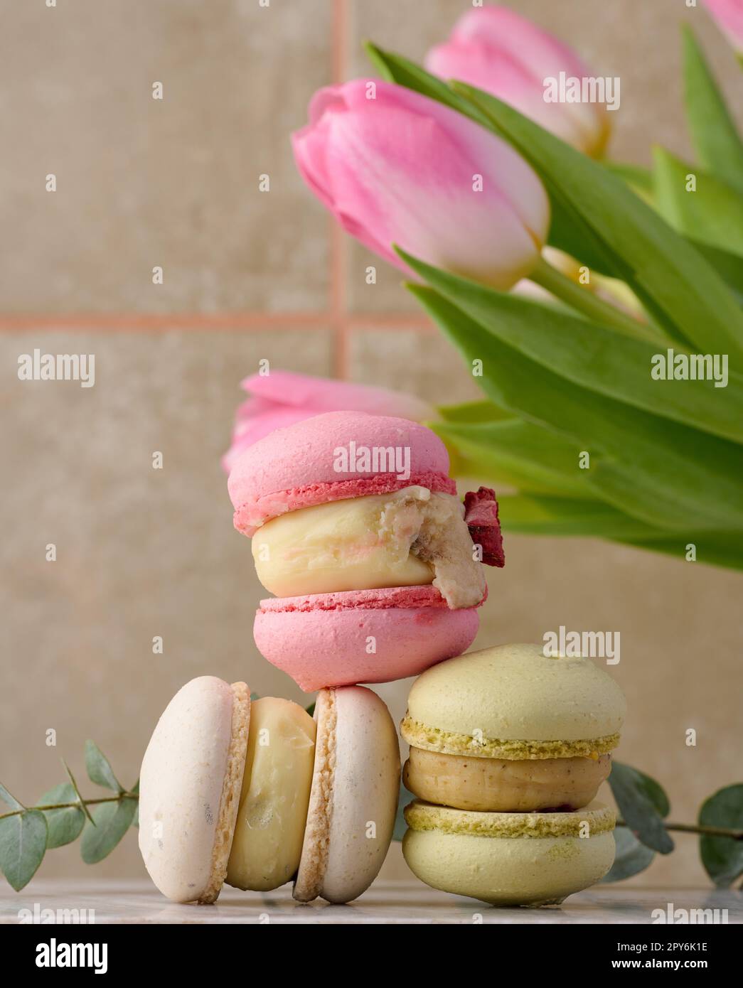 Baked macarons with different flavors on the table, behind a bouquet of tulips Stock Photo
