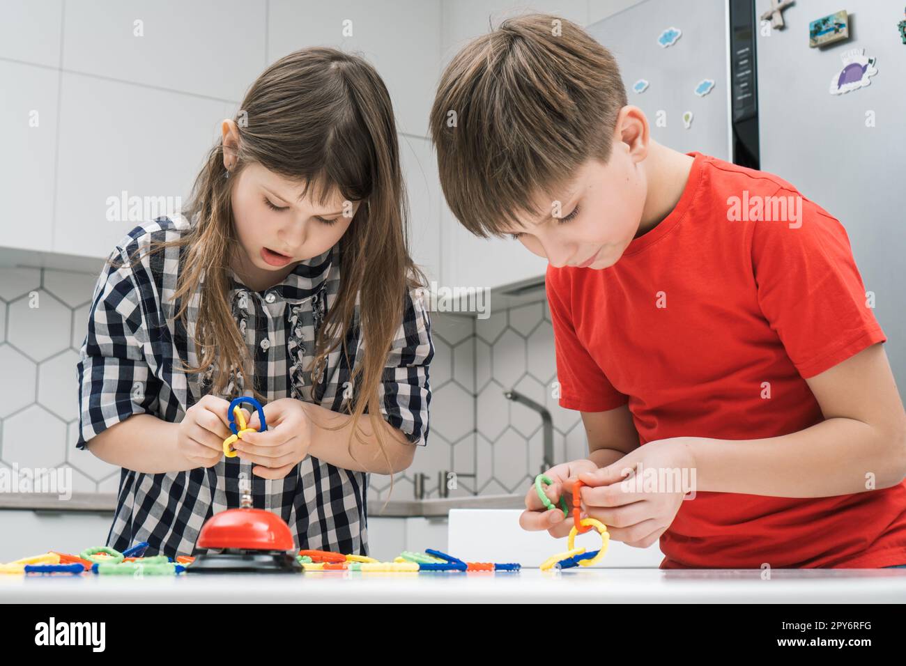 Kids play toy constructor standing above kitchen table and looking down. Boy and girl collect plastic details of lego. Stock Photo