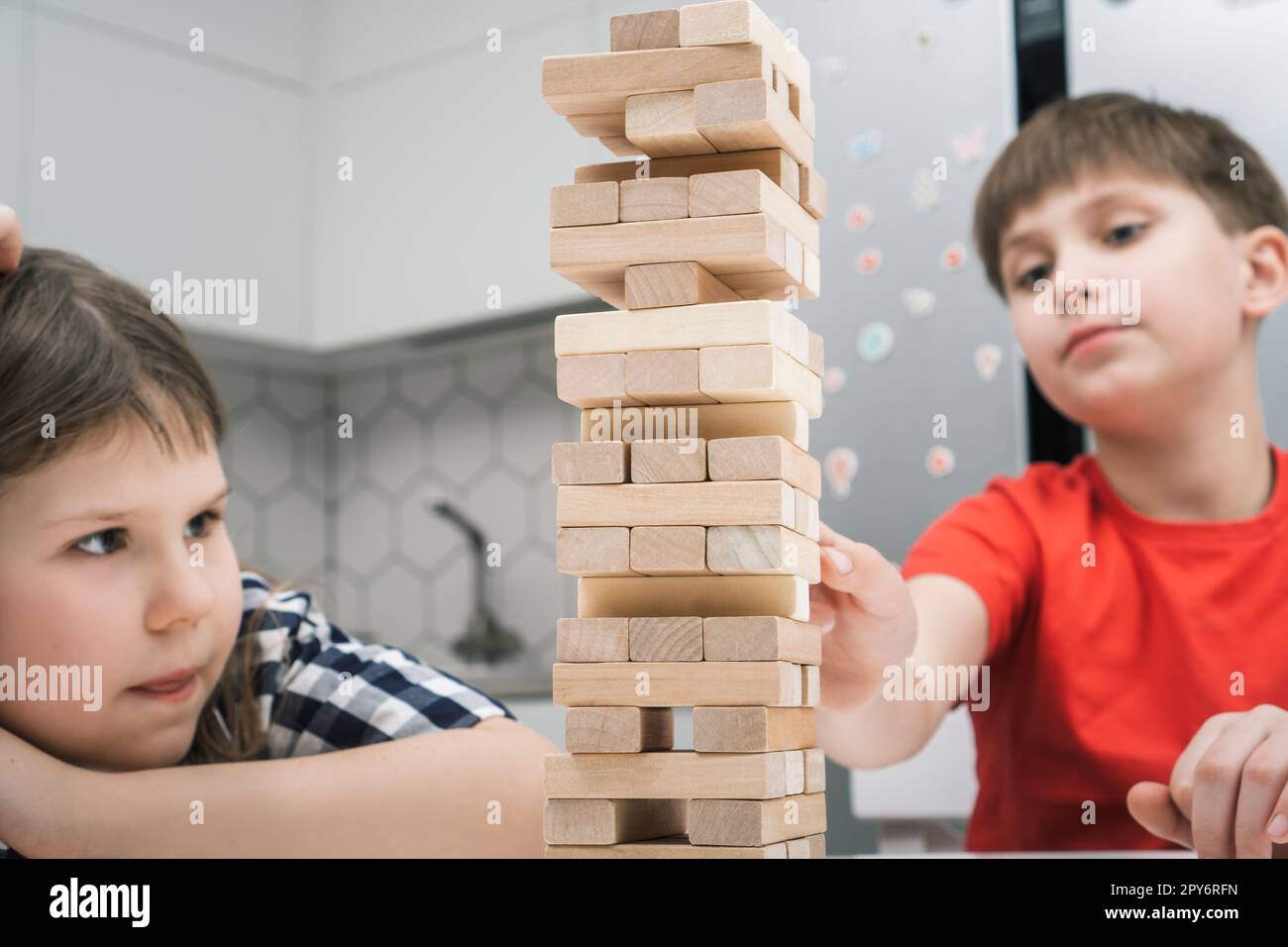 School kids play tower sitting at table closeup. Boy and girl build tower from little wooden blocks keeping balance. Stock Photo