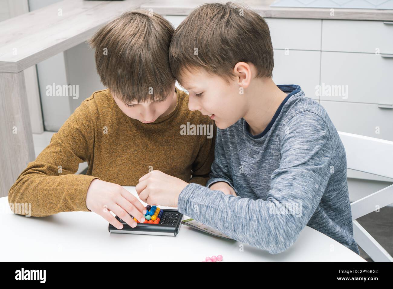 Happy schoolboys play toy constructor sitting at table. Children collect colored details on playing board. Board games. Stock Photo