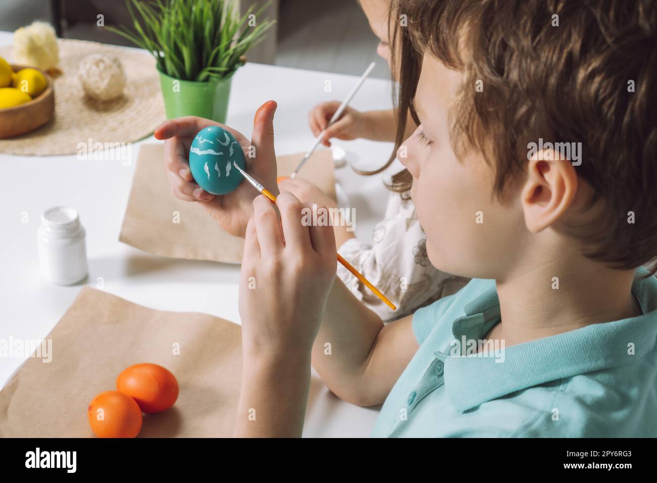 Cropped portrait of boy hand, painting multi coloring Easter hens eggs, brown paper plate table, paintbrush Stock Photo