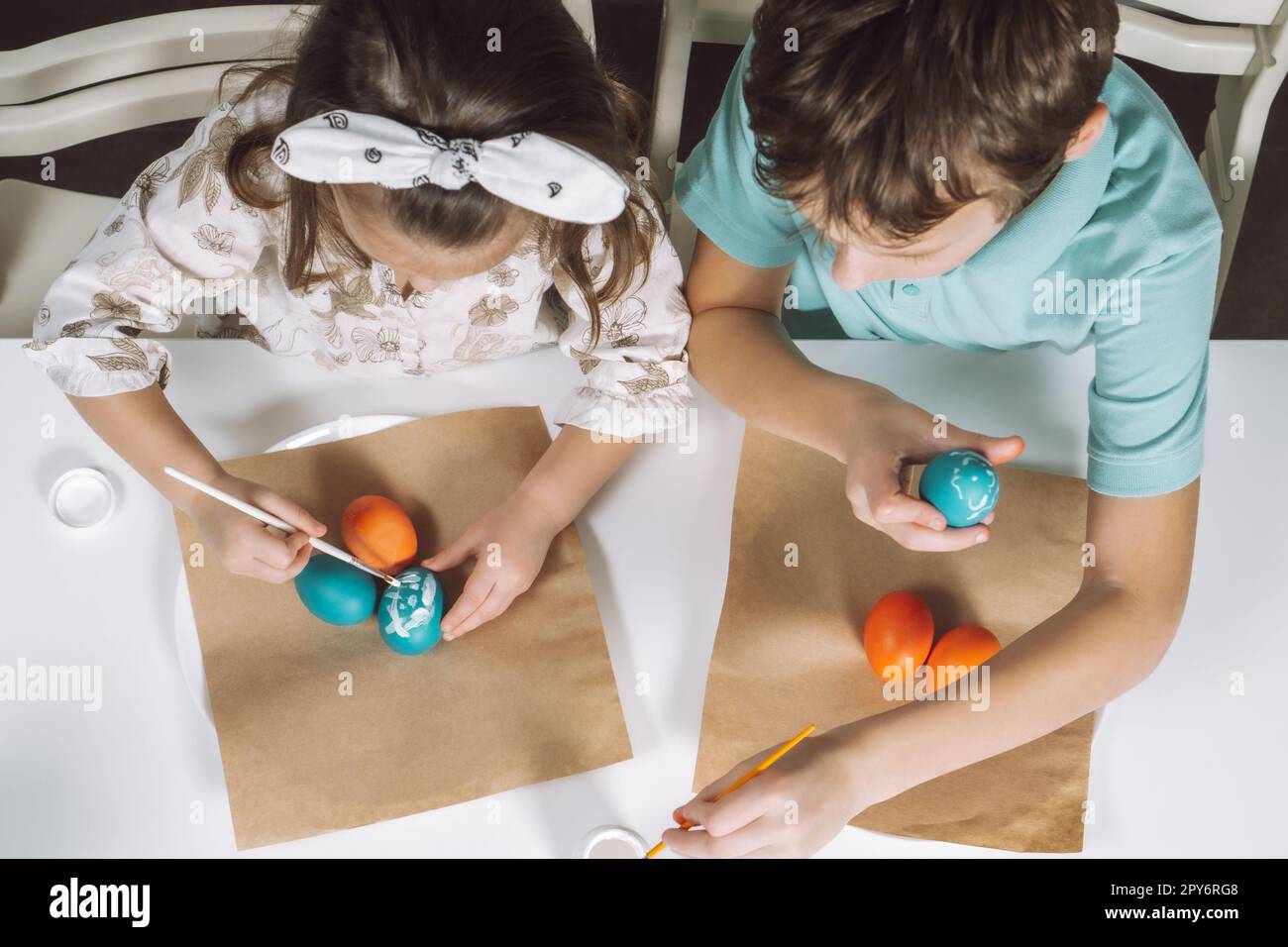 Portrait two children, little girl, boy siblings, painting multi coloring Easter eggs in kitchen, paintbrush. Top view Stock Photo