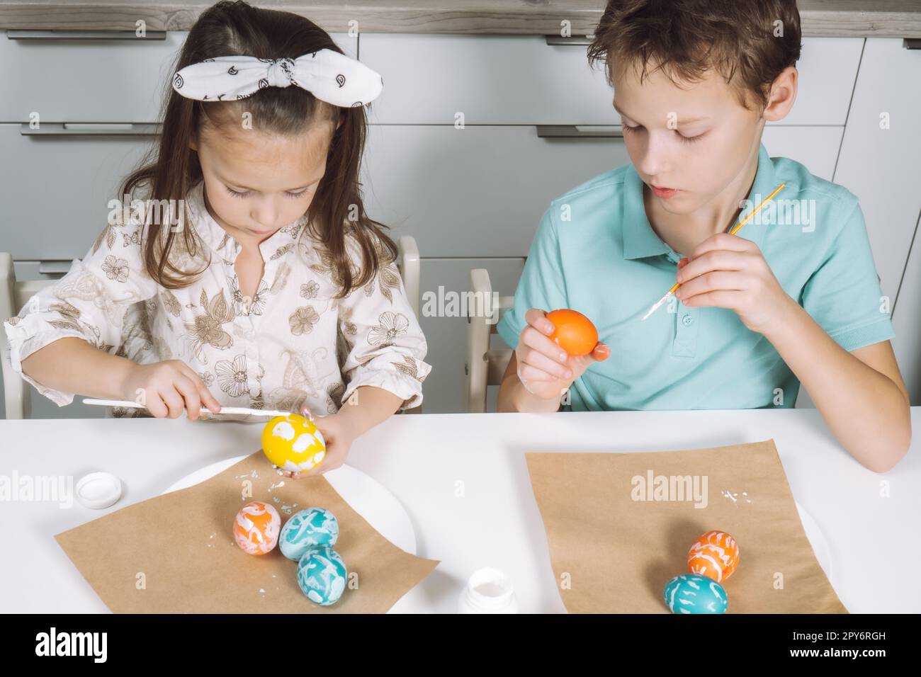 Portrait two children, little girl, boy siblings, painting multi coloring Easter eggs in kitchen, paintbrush. Top view Stock Photo