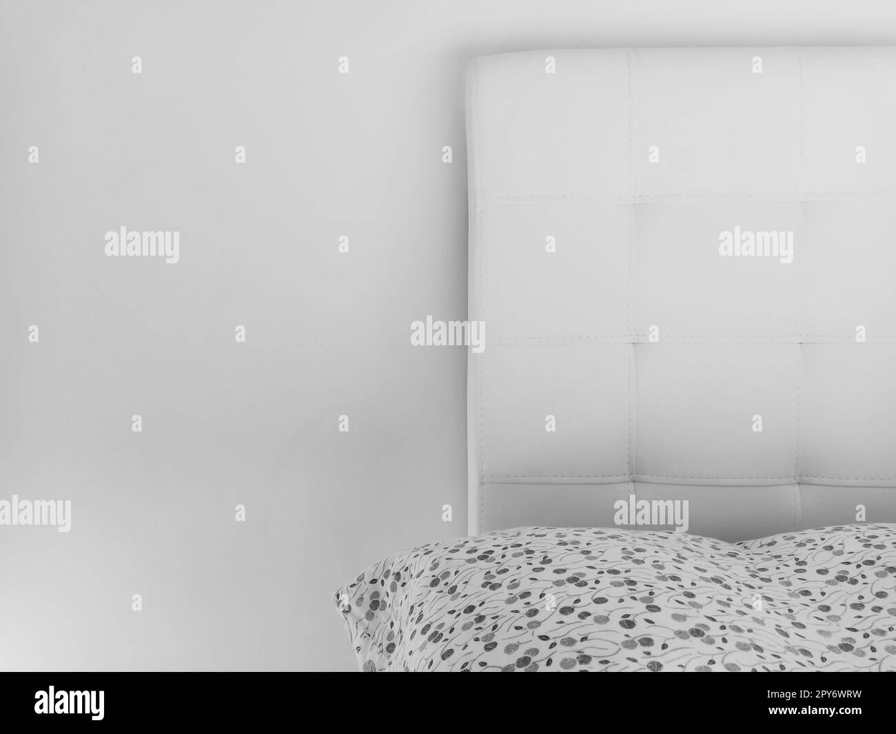 Soft headboard. Upholstery for furniture made of genuine or artificial leather and quilted fabric. Soft headboard against a light wall. Black and white monochrome photo Stock Photo