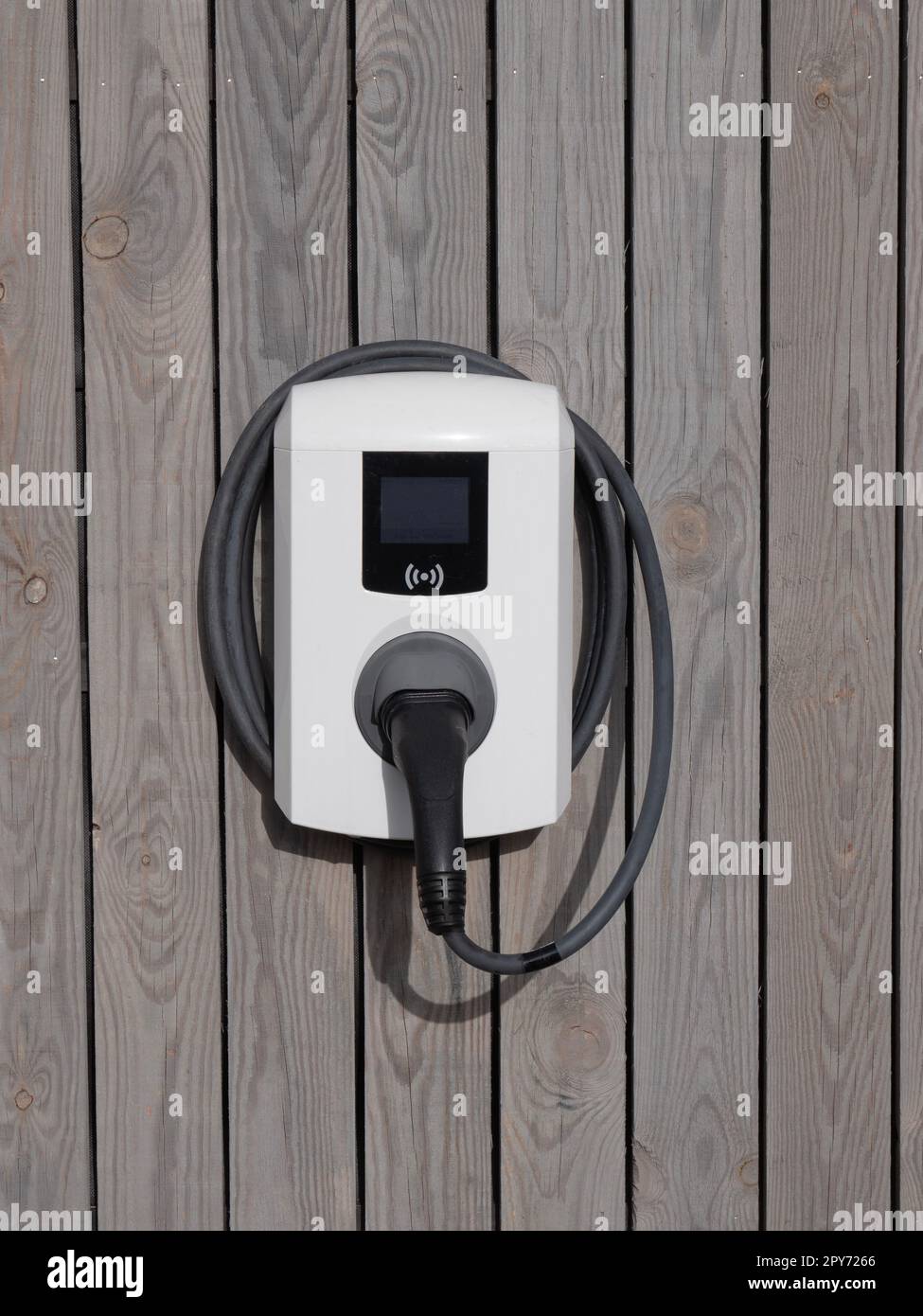 A white private charger for electric cars against a wooden wall Stock Photo
