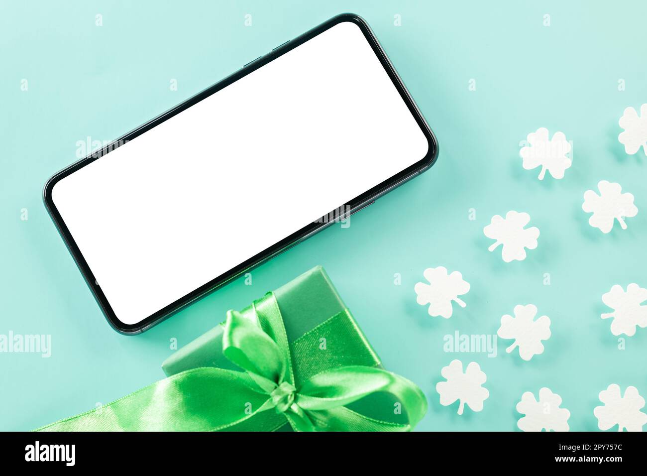 overhead flat lay of paper cut clover leaves festive decor and mobile phone blank screen Stock Photo