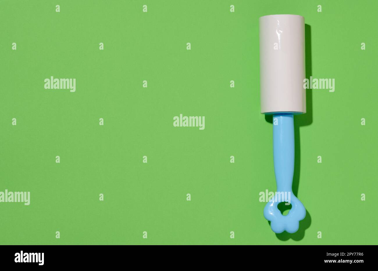 Roller with sticky tape for cleaning clothes on a green background, top view Stock Photo