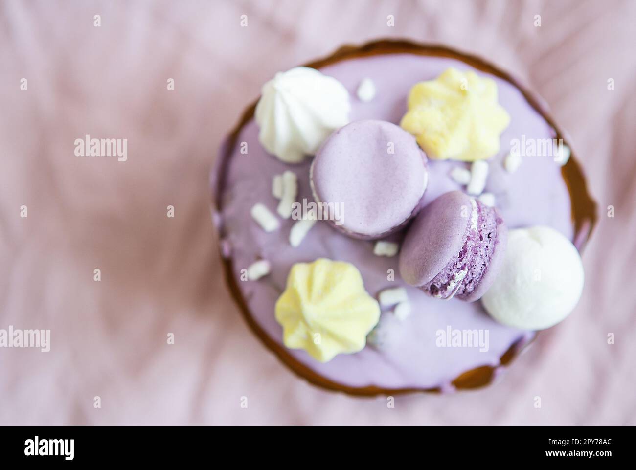 A traditional paska decorated with white Swiss chocolate and meringue stands on a lavender tablecloth. Easter holiday, top view. Place for inscription. Stock Photo