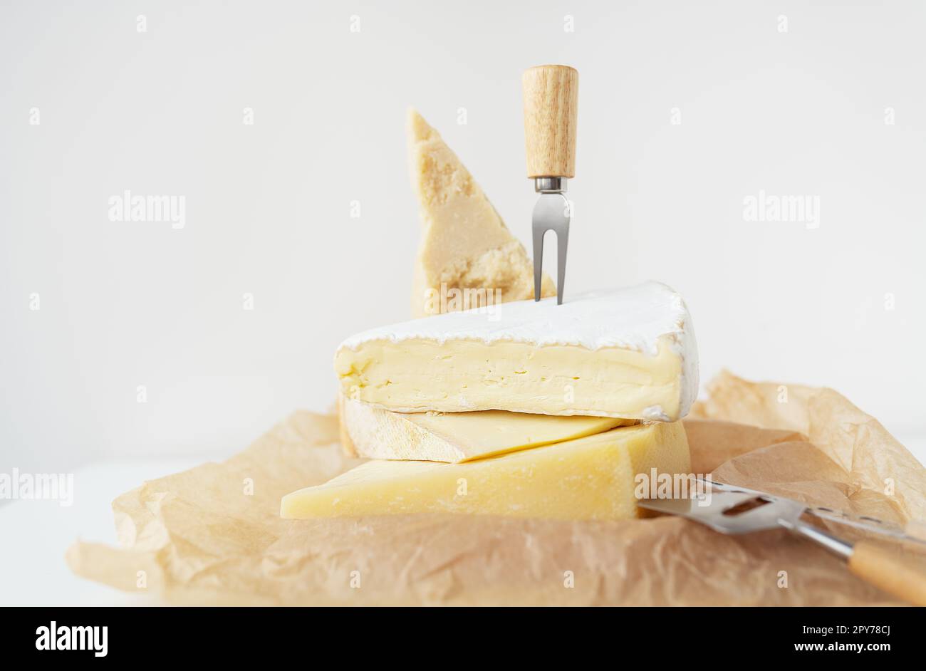 Different types of cheese lie on top of each other with cheese knives on parchment. A delicious delicacy. Stock Photo