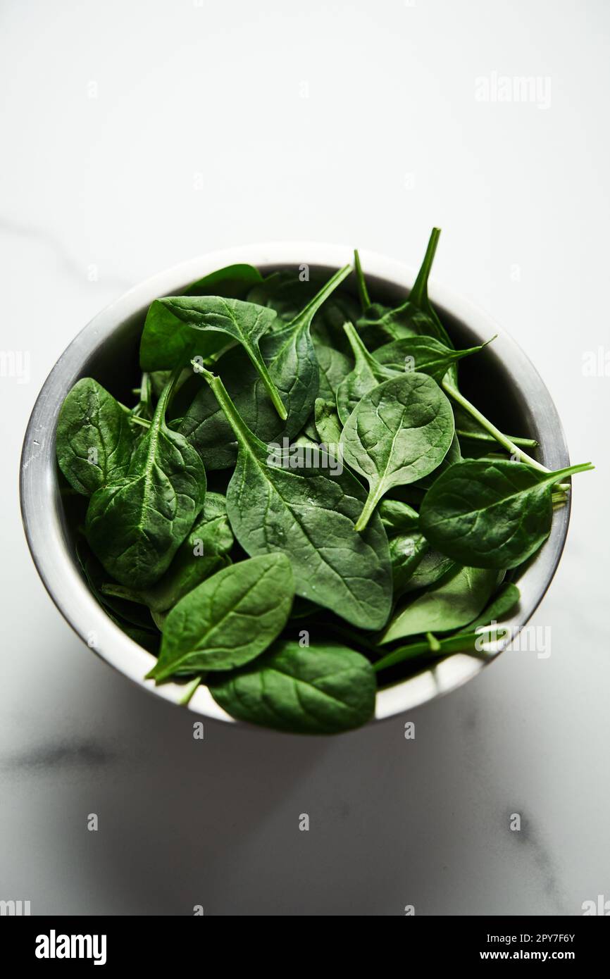 A bunch of Fresh baby spinach leaves in the in a stainless steel bowl on white marble background. Stock Photo