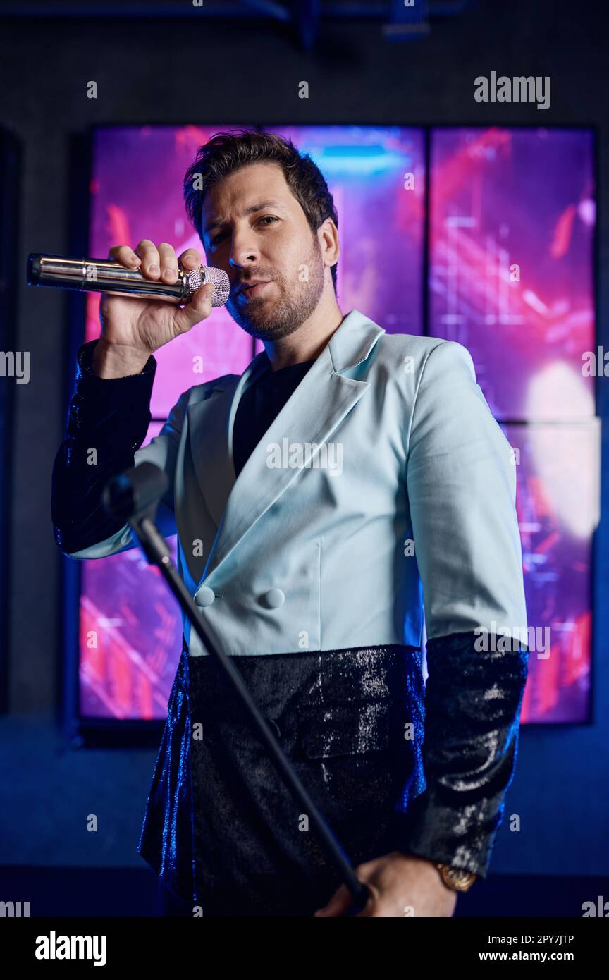 Male singer holding microphone standing and performing on stage Stock Photo