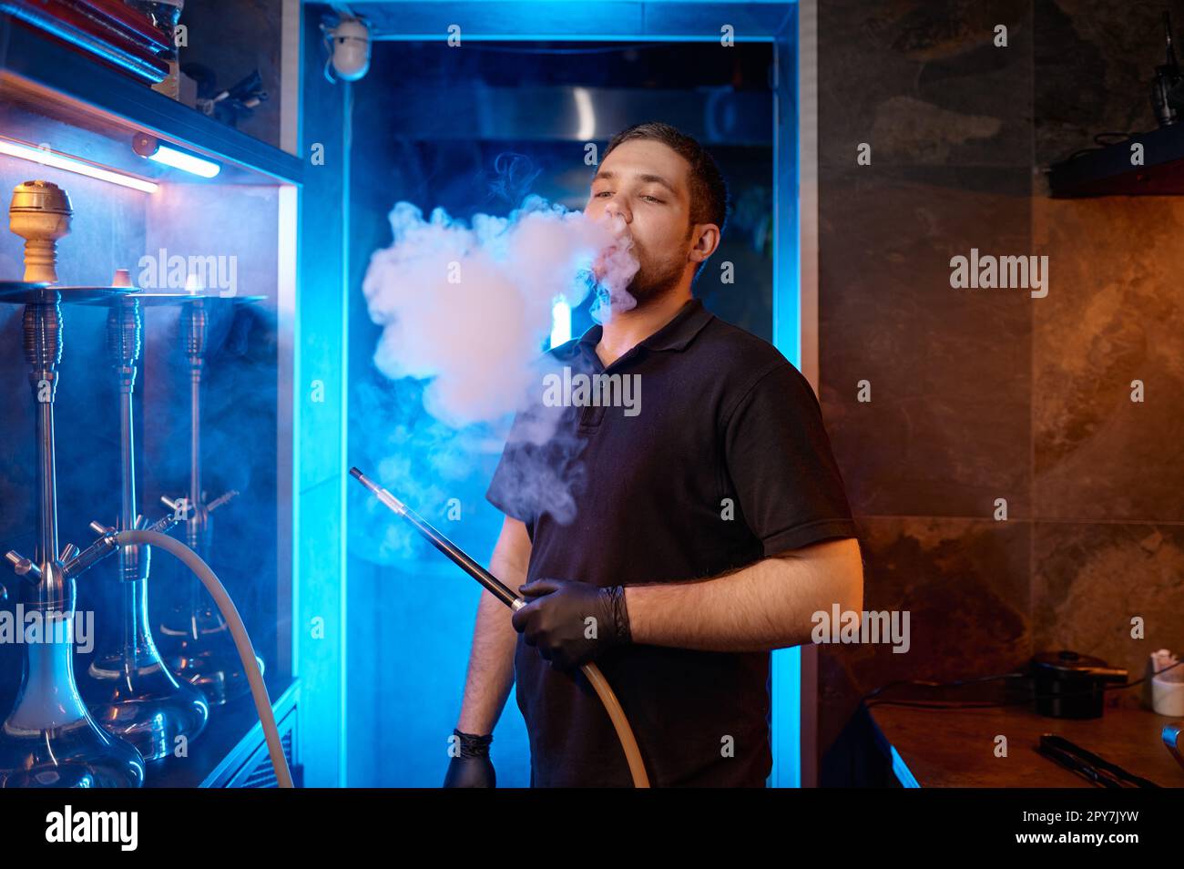 Young man smoking at hookah bar while preparing equipment for client