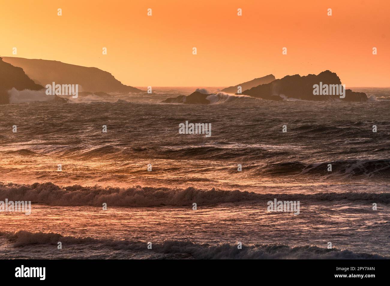 Late evening golden light over the headlands and the two rocky uninhabited islands in Fistral Bay in Newquay in Cornwall in the UK. Stock Photo