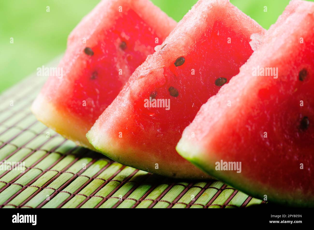 Closeup of sweet red watermelon slices on green table background in garden with sunlight. Stock Photo