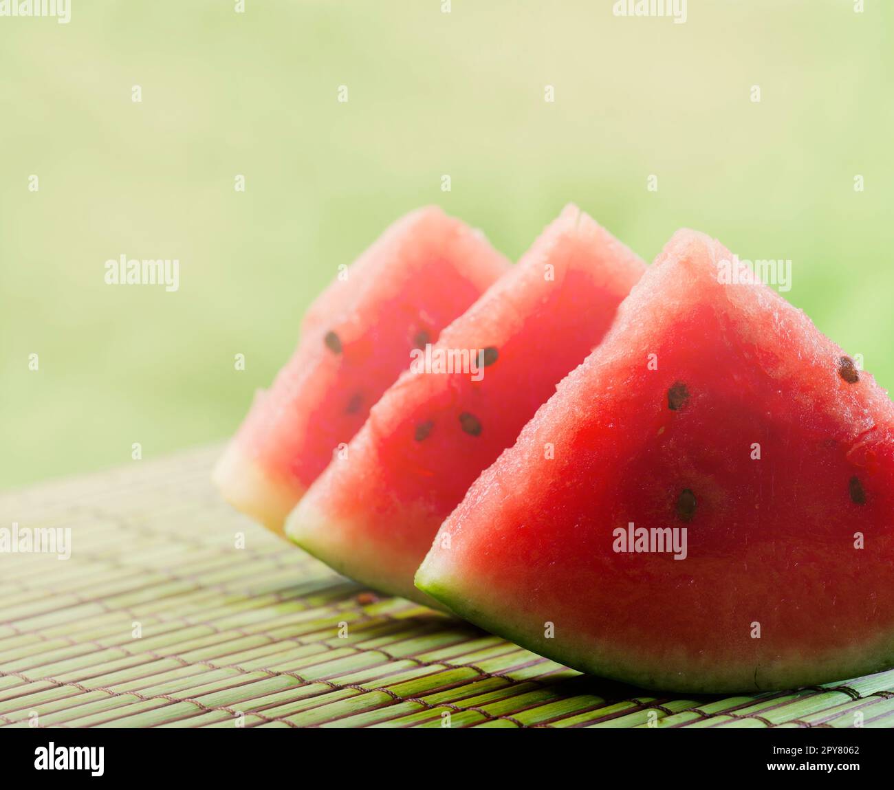 Closeup of sweet red watermelon slices on green table background in garden with sunlight. Stock Photo