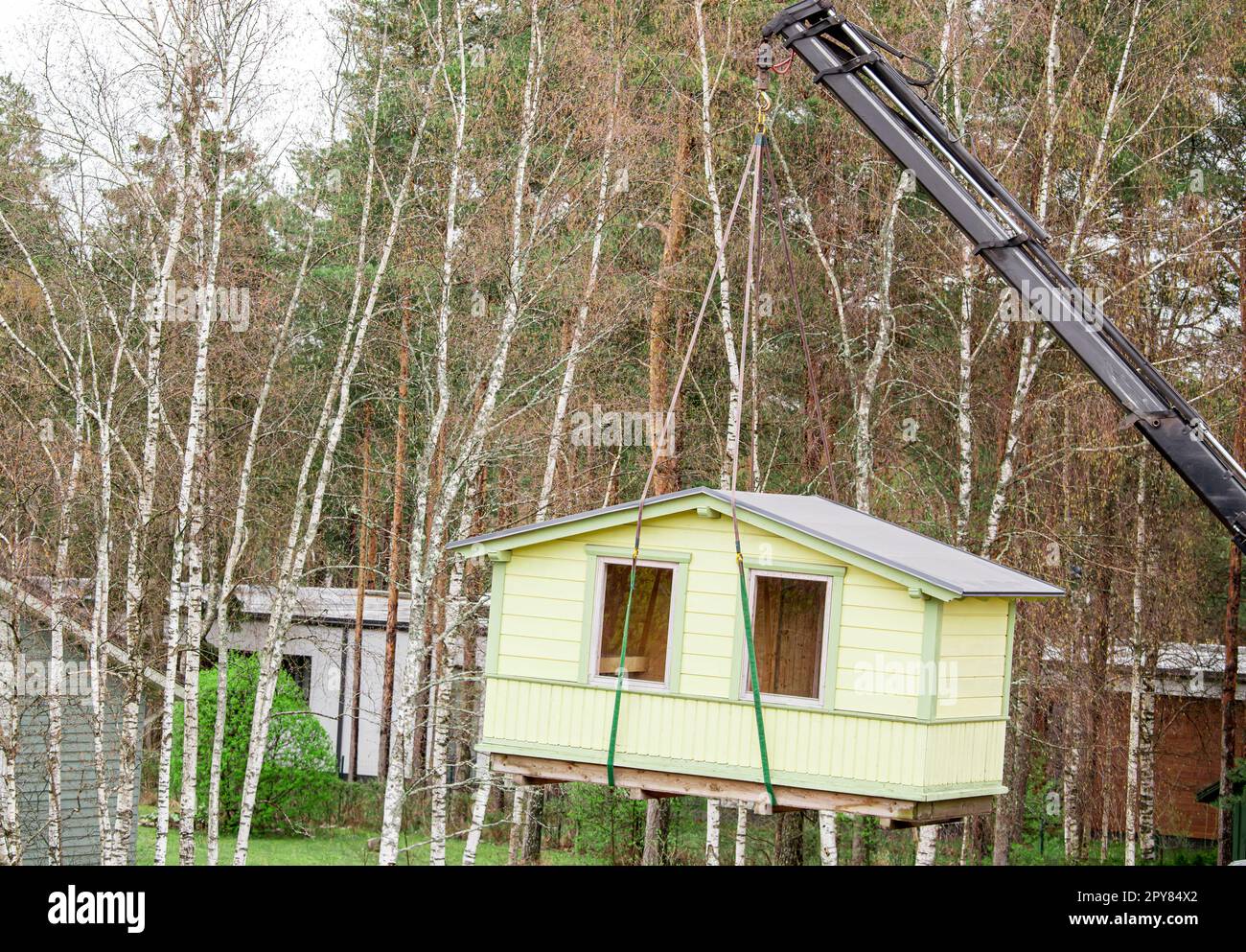 Crane lifting up the tiny house outdoors in spring in nature. Stock Photo