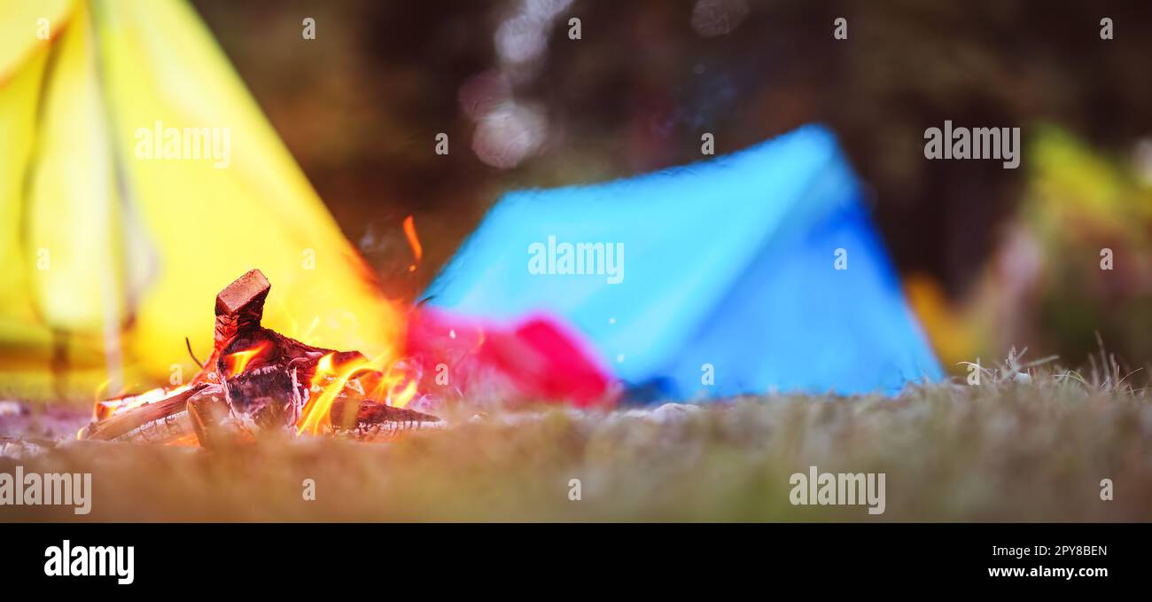 Closeup view of the fireplace near colourful tents in wilderness park. Stock Photo
