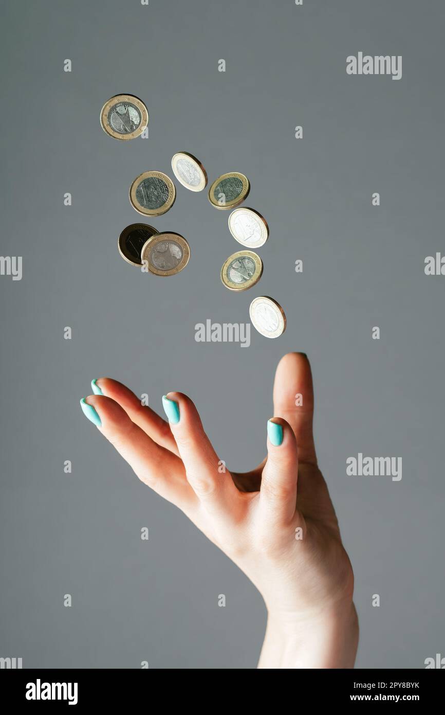 Female hand throwing money, one euro coins into air on gray background