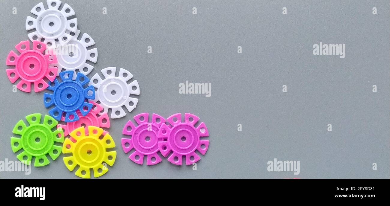 Multi-colored details in the form of snowflakes from the childrens designer on a gray background.Red, yellow, green, blue, white, pink plastic discs for the development of fine motor skills of fingers Stock Photo