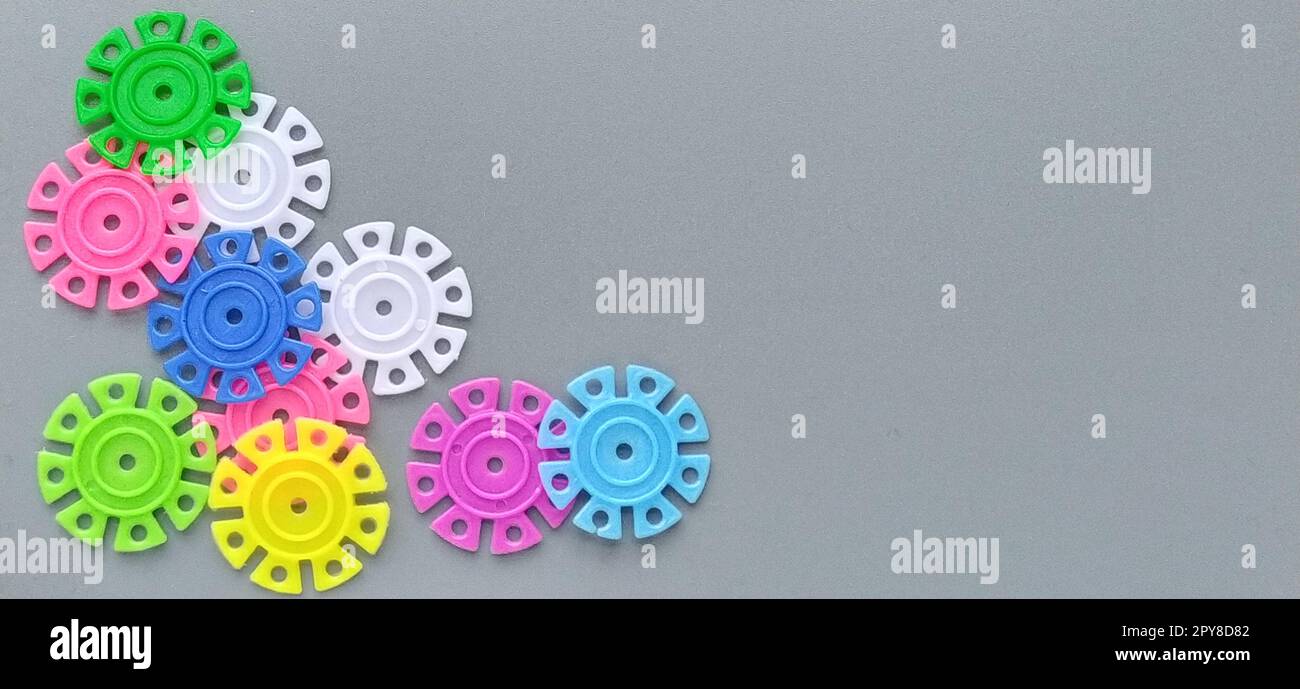 Multi-colored details in the form of snowflakes from the childrens designer on a gray background.Red, yellow, green, blue, white, pink plastic discs for the development of fine motor skills of fingers Stock Photo