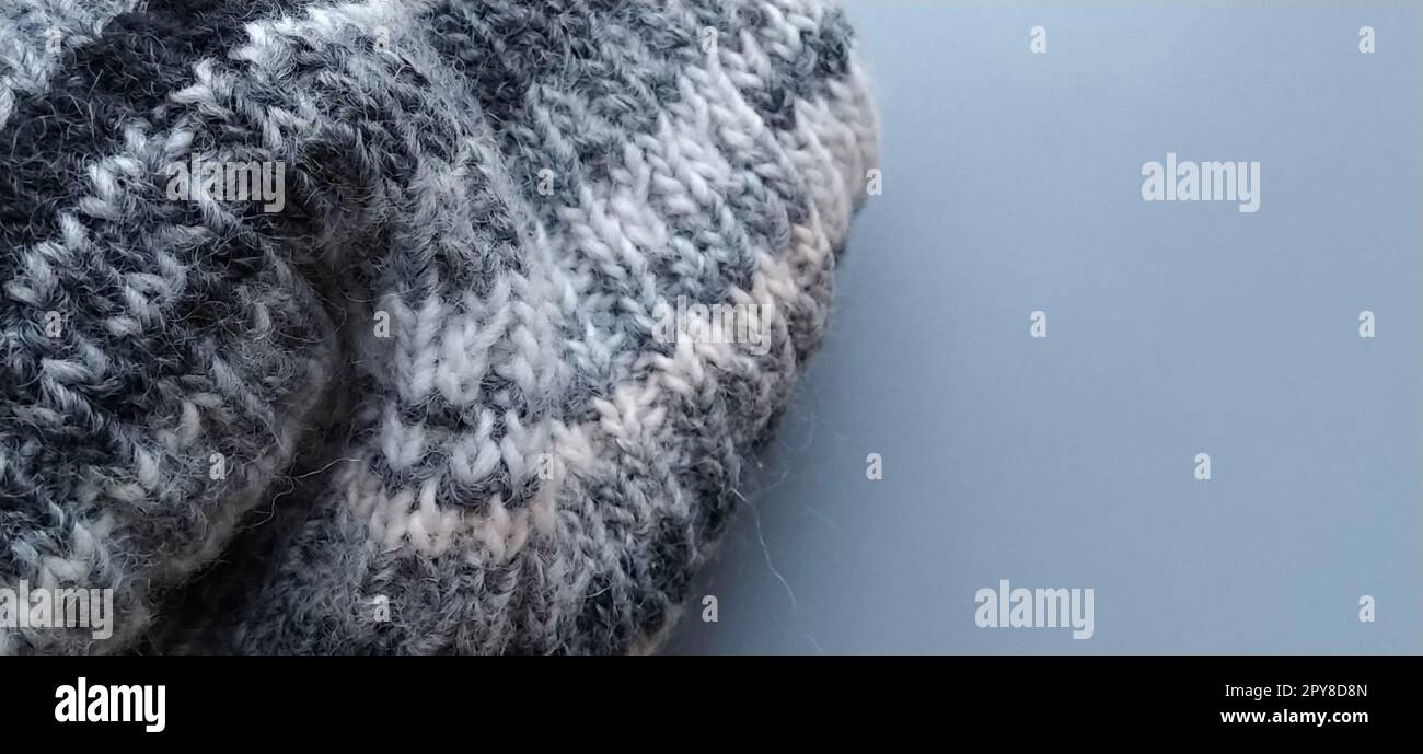 Knitted warm product such as a scarf or hat on a gray background. Knitting with multi-colored yarn. White, gray, brown, beige and black stripes and patterns on winter clothes. Stock Photo