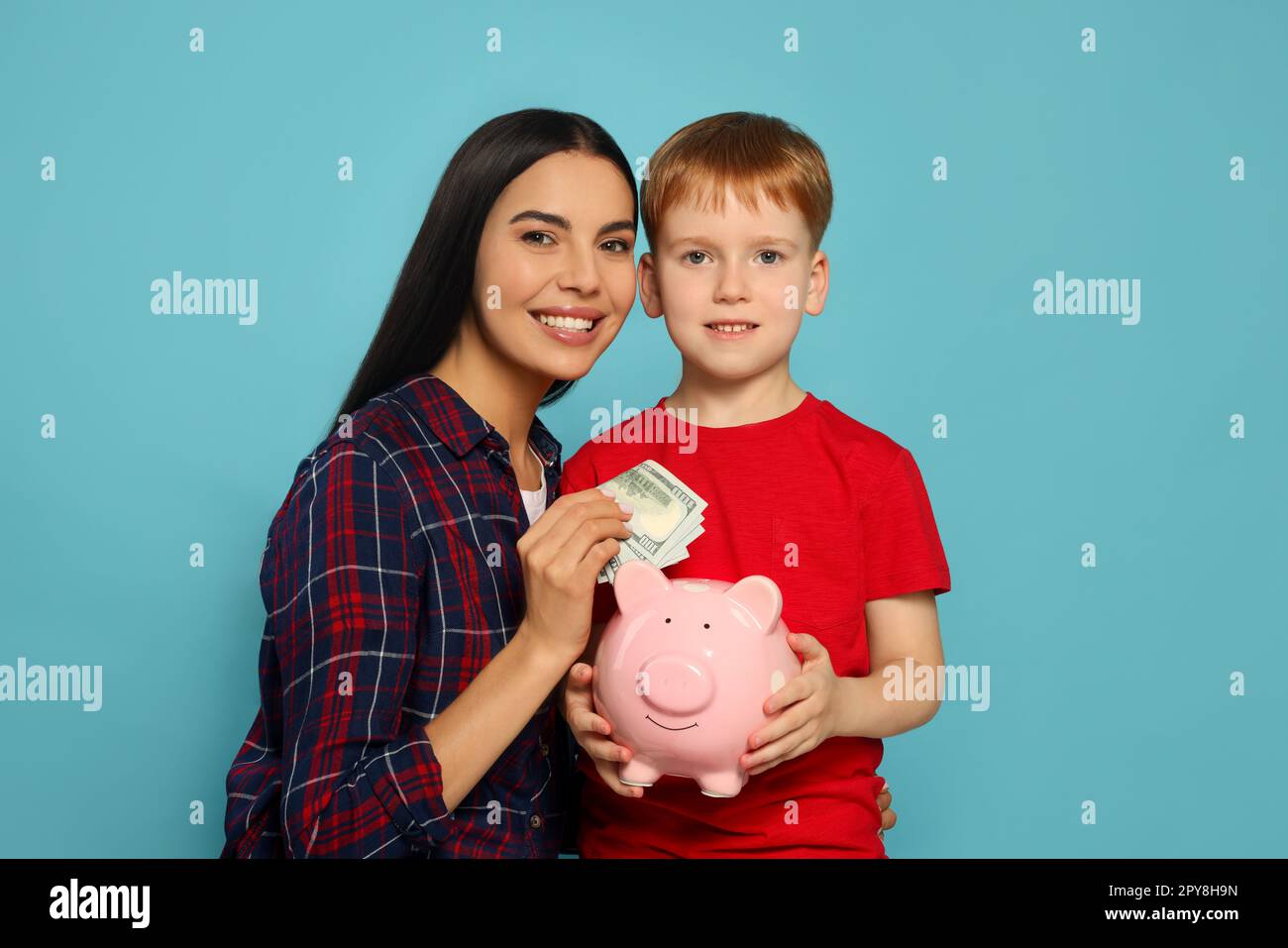 Mother and her son putting money into piggy bank on light blue ...
