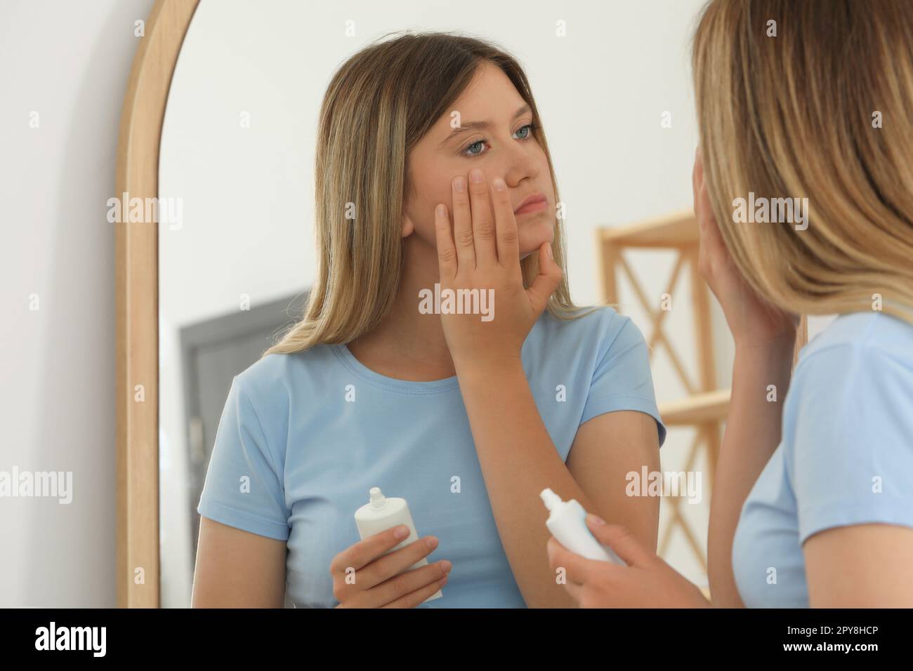 Sleep deprived young woman covering up dark circles with concealer near